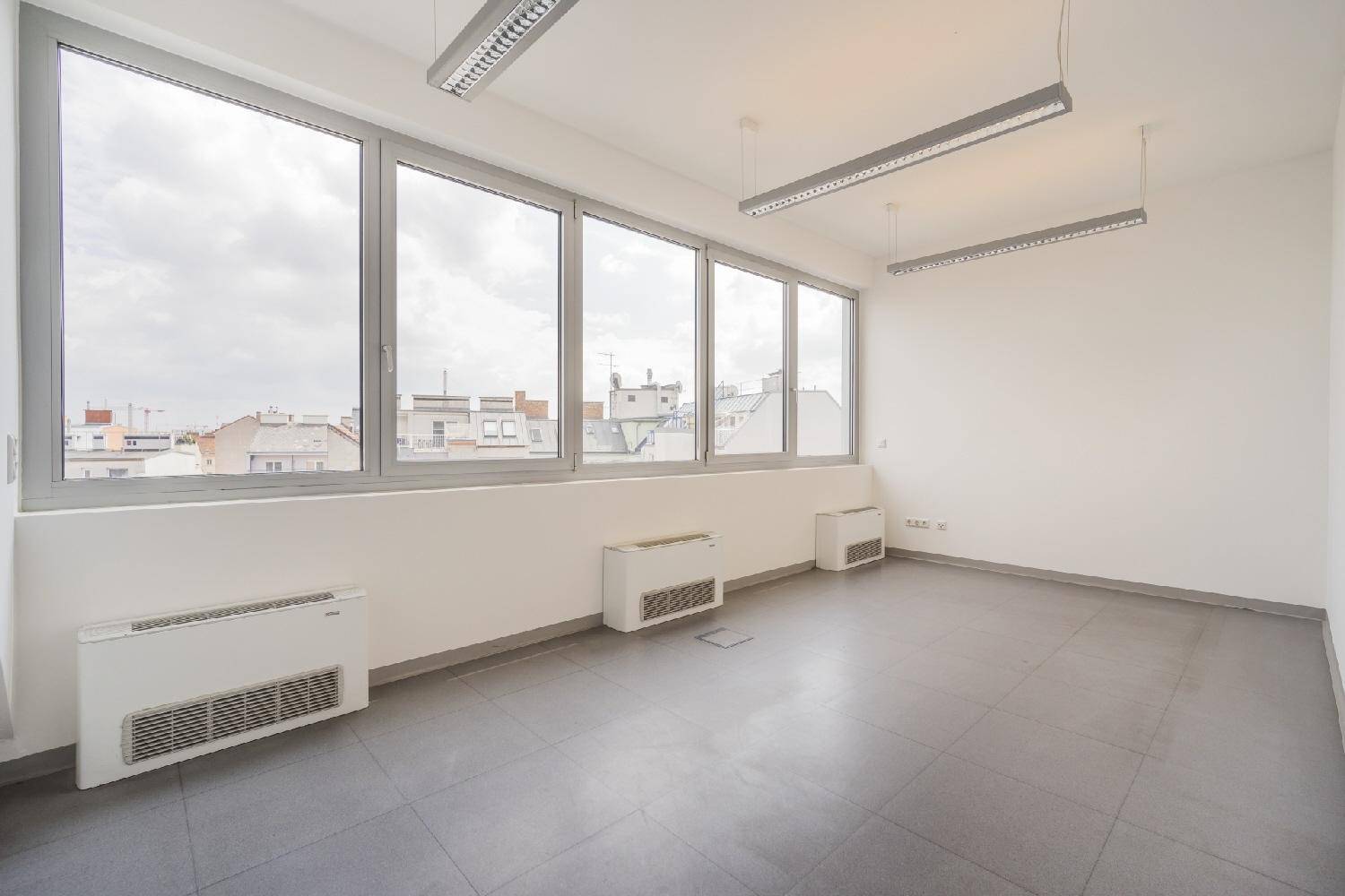 Heller Büroraum mit einer Fensterfront, grauen Fliesen und Blick auf die städtische Umgebung.