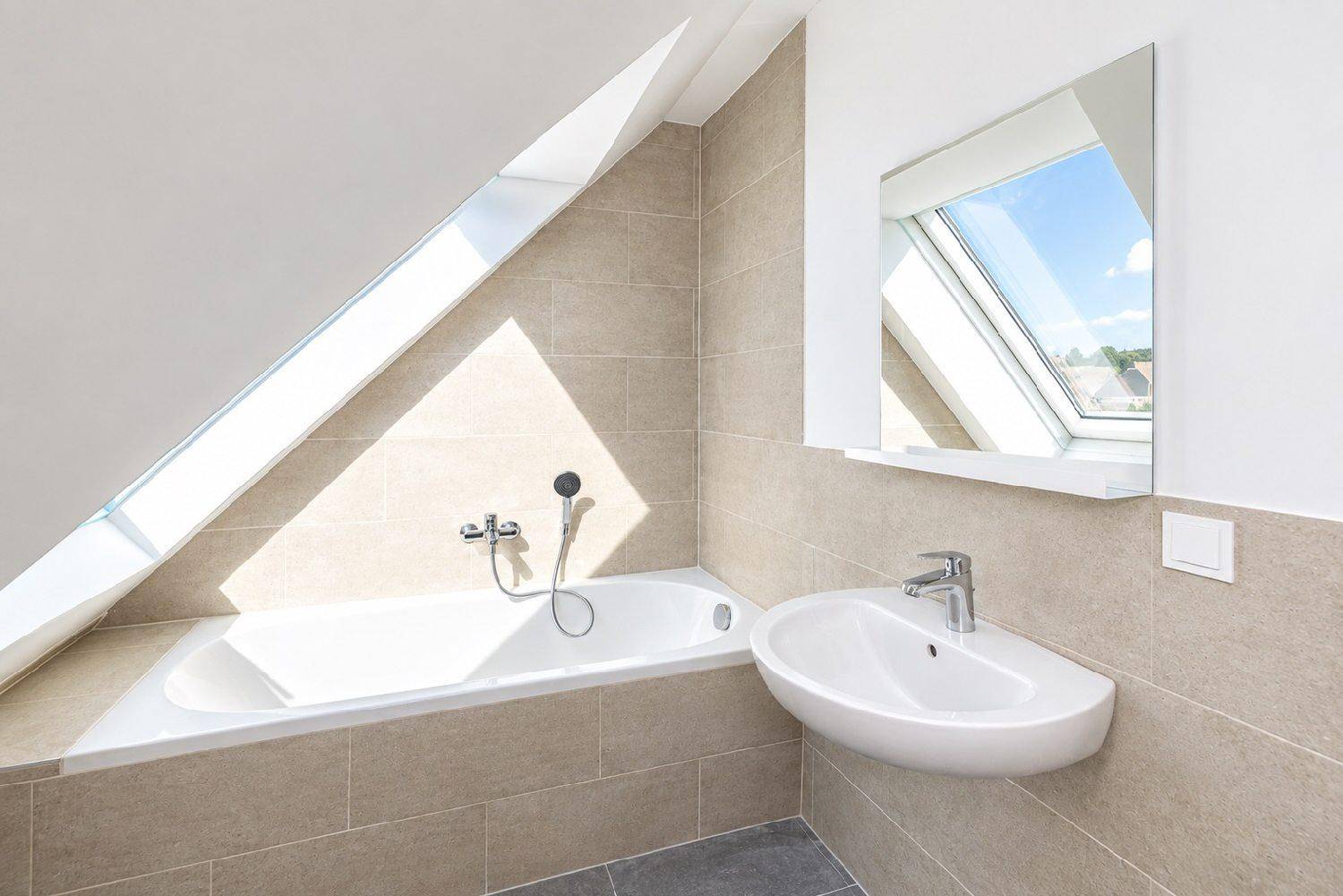 Modernes Badezimmer mit beigen Fliesen, Badewanne, Waschbecken und einem Dachfenster für Tageslicht.