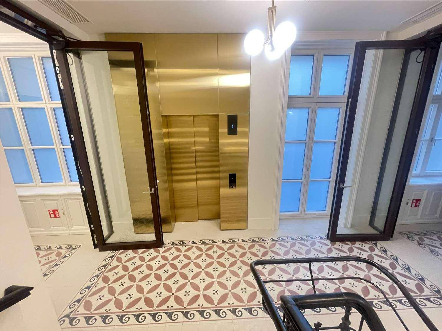 Eingangsbereich mit modernem goldenem Aufzug, großen Fenstern und dekorativen Bodenfliesen.