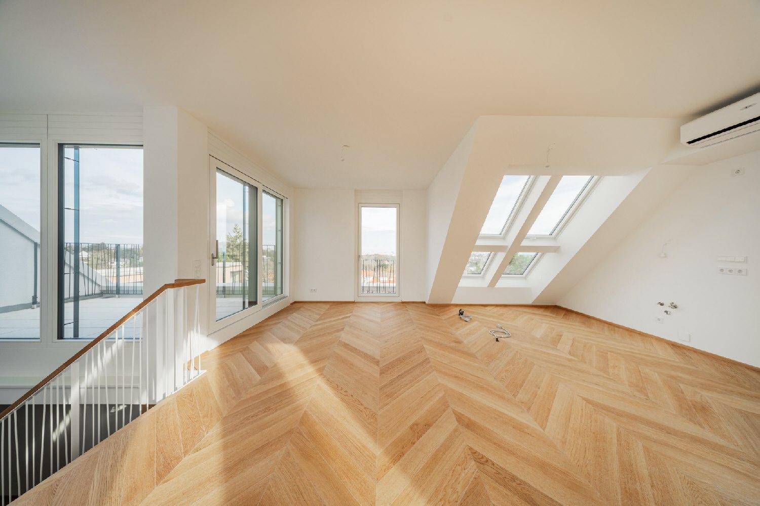 Geräumiges Dachgeschosszimmer mit hellem Fischgrätparkett, großen Fenstern und Zugang zu einem Balkon.