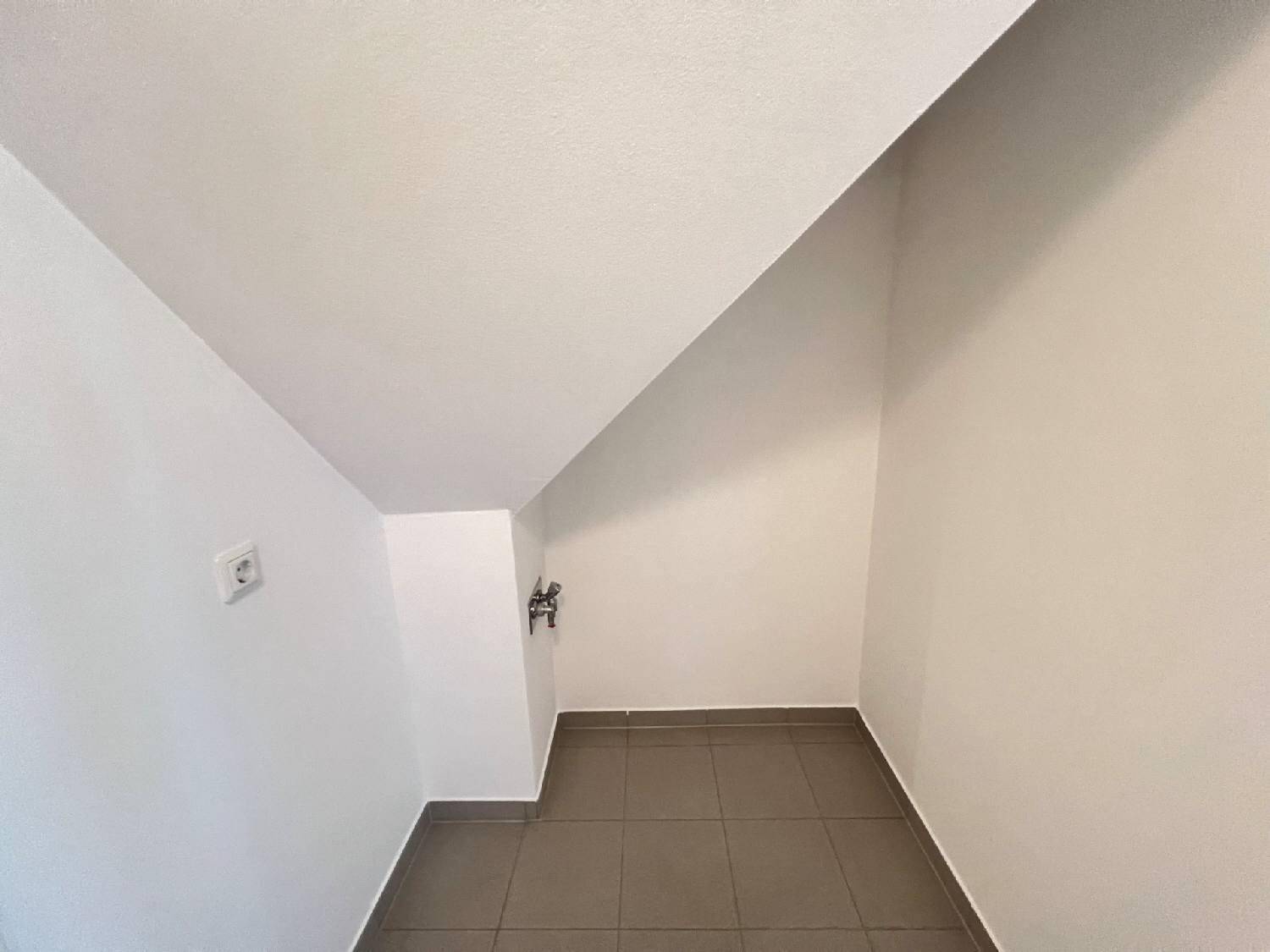 Kleiner Abstellraum mit Fliesenboden und Anschlüssen unter der Dachschräge.