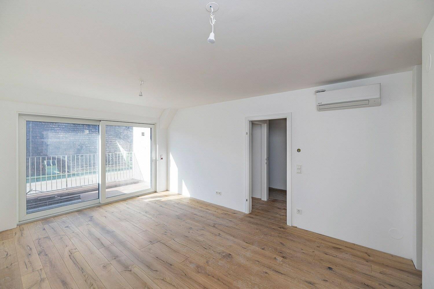 Helles Wohnzimmer im Neubau mit Holzboden, Klimaanlage und Zugang zum Balkon.