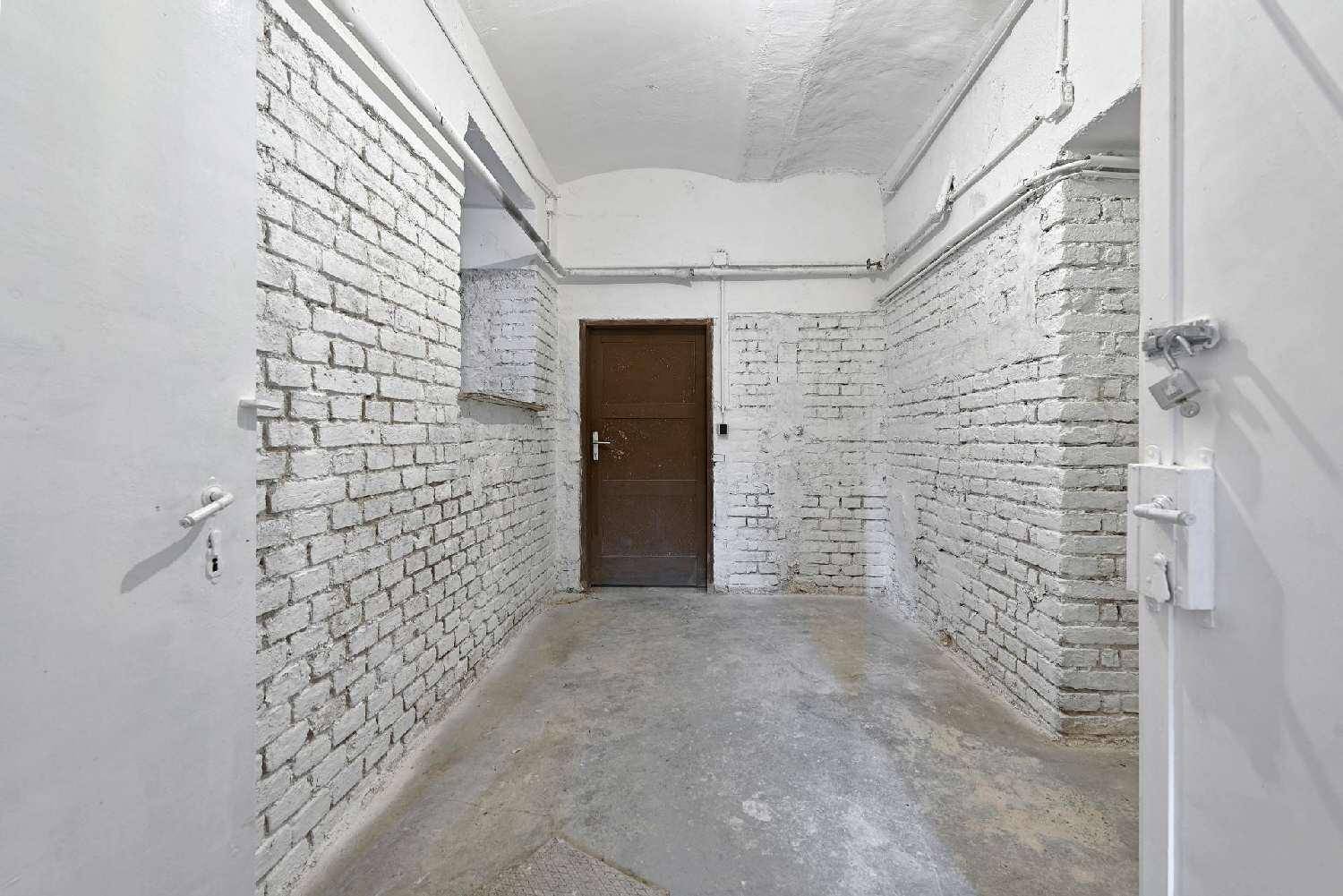 Schmaler Flur mit weiß gestrichenen Ziegelwänden, Betonboden und einer dunklen Holztür am Ende.