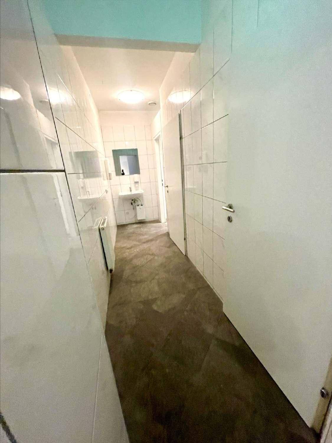Heller Flur mit weißen Fliesenwänden und dunklem Boden, führt zu einem Badezimmer.