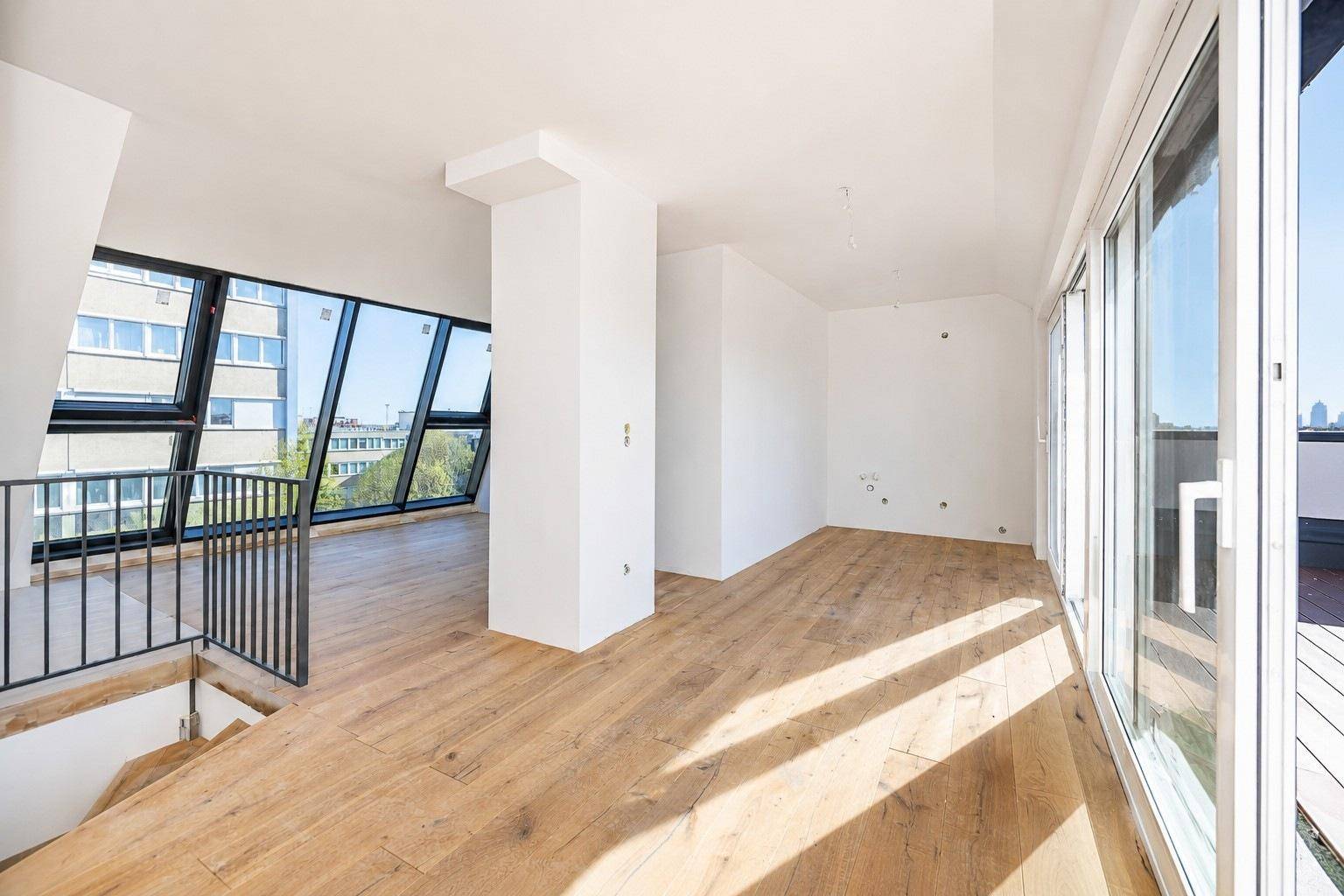 Heller, offener Wohnbereich mit großen Fenstern, Holzboden und Zugang zu einer Terrasse.