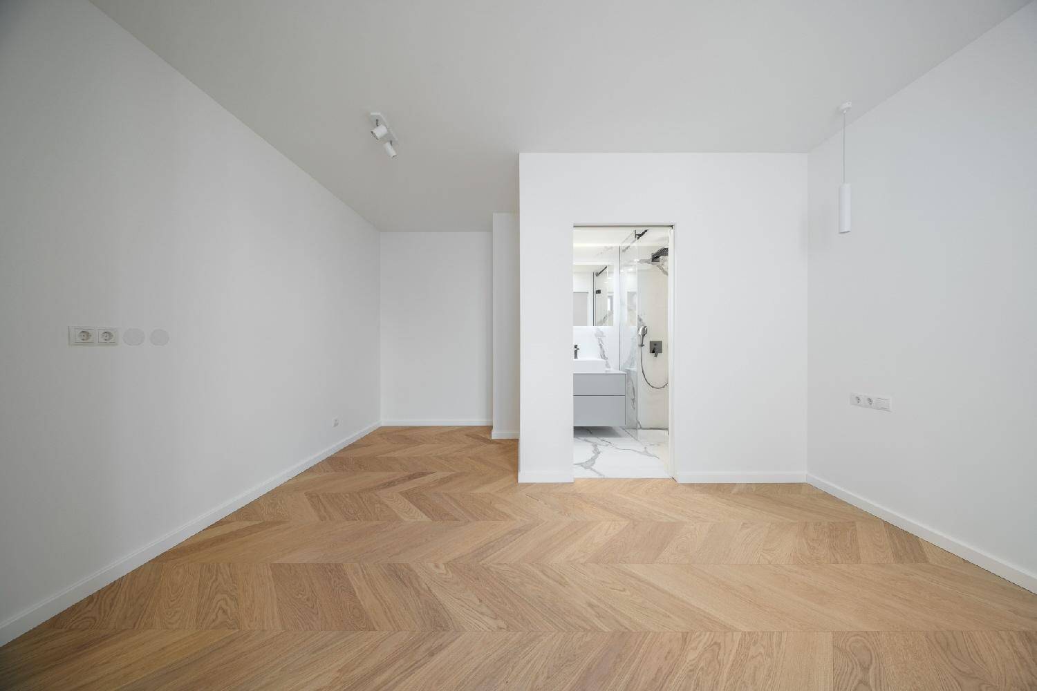 Geräumiges Zimmer mit Fischgrätparkett und Blick auf ein modernes Badezimmer mit Marmorfliesen.