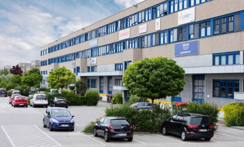 Fassade eines modernen Bürogebäudes mit zahlreichen Fenstern und einem gut genutzten Parkplatz davor.
