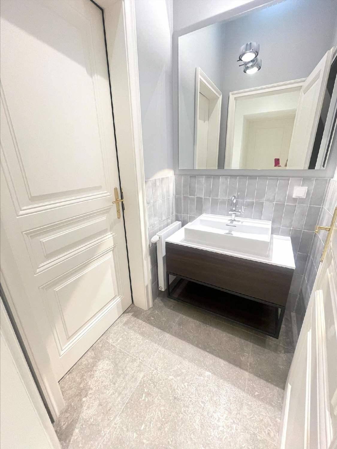 Elegantes Badezimmer mit modernem Waschtisch, großem Spiegel und grauen Wand- und Bodenfliesen.