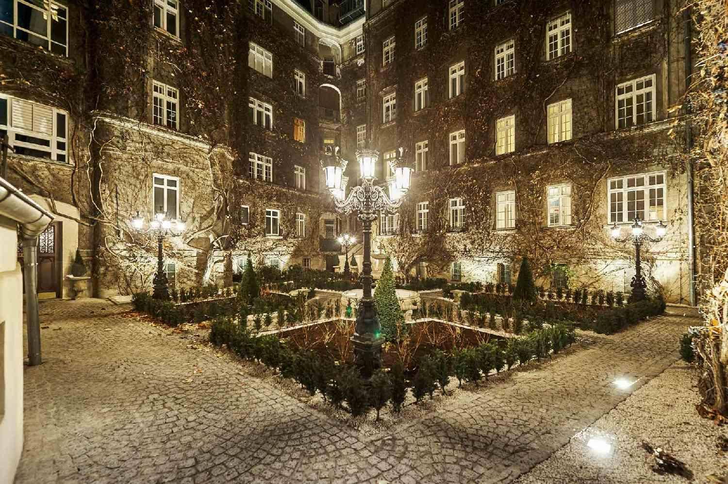 Romantischer Innenhof bei Nacht mit beleuchtetem Brunnen und gepflegten Pflanzen.