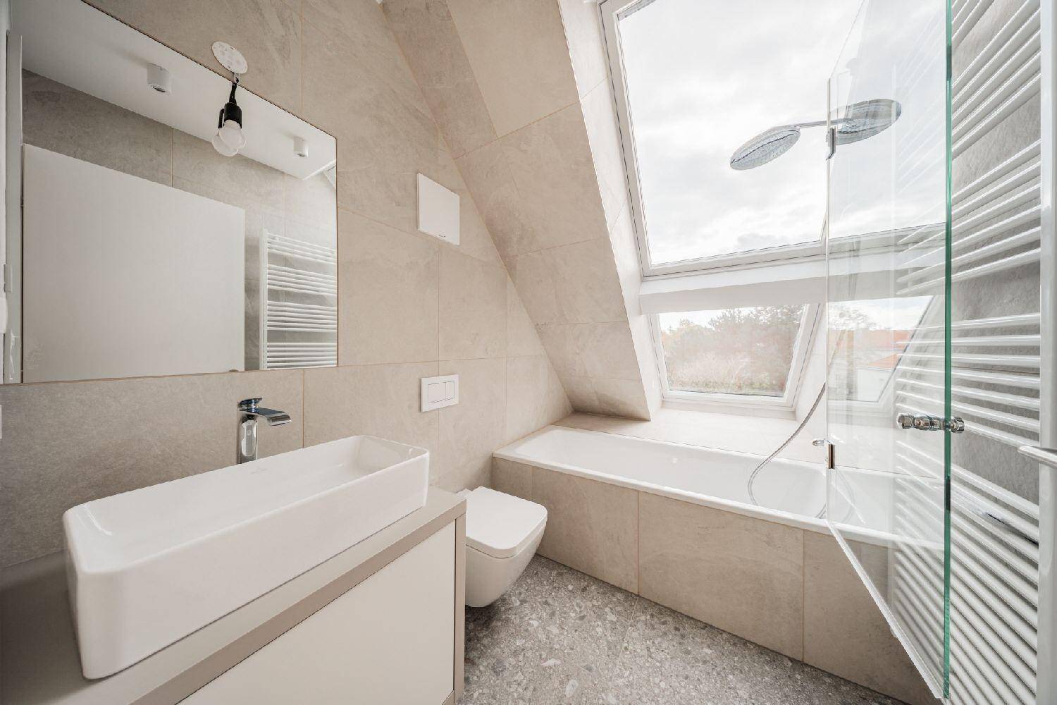 Modernes Badezimmer mit Badewanne, Dusche, Dachfenster und hellen Fliesen im Neubau.