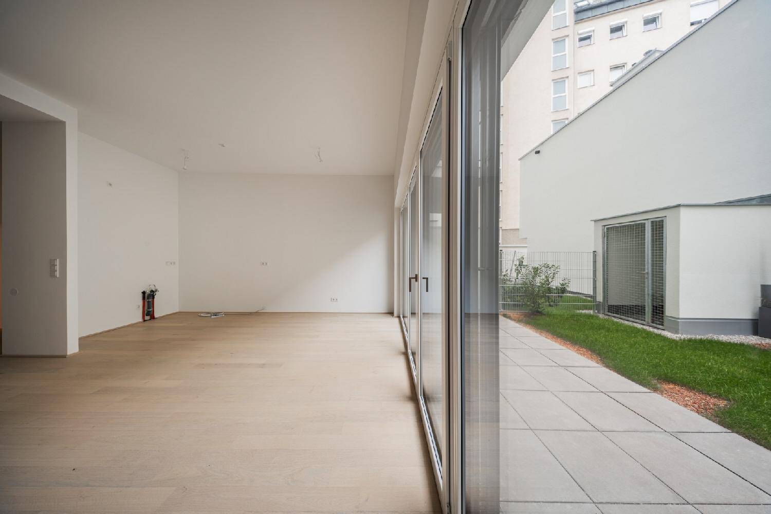 Geräumiger, unmöblierter Wohnbereich mit breiter Fensterfront und Blick auf die Außenterrasse.
