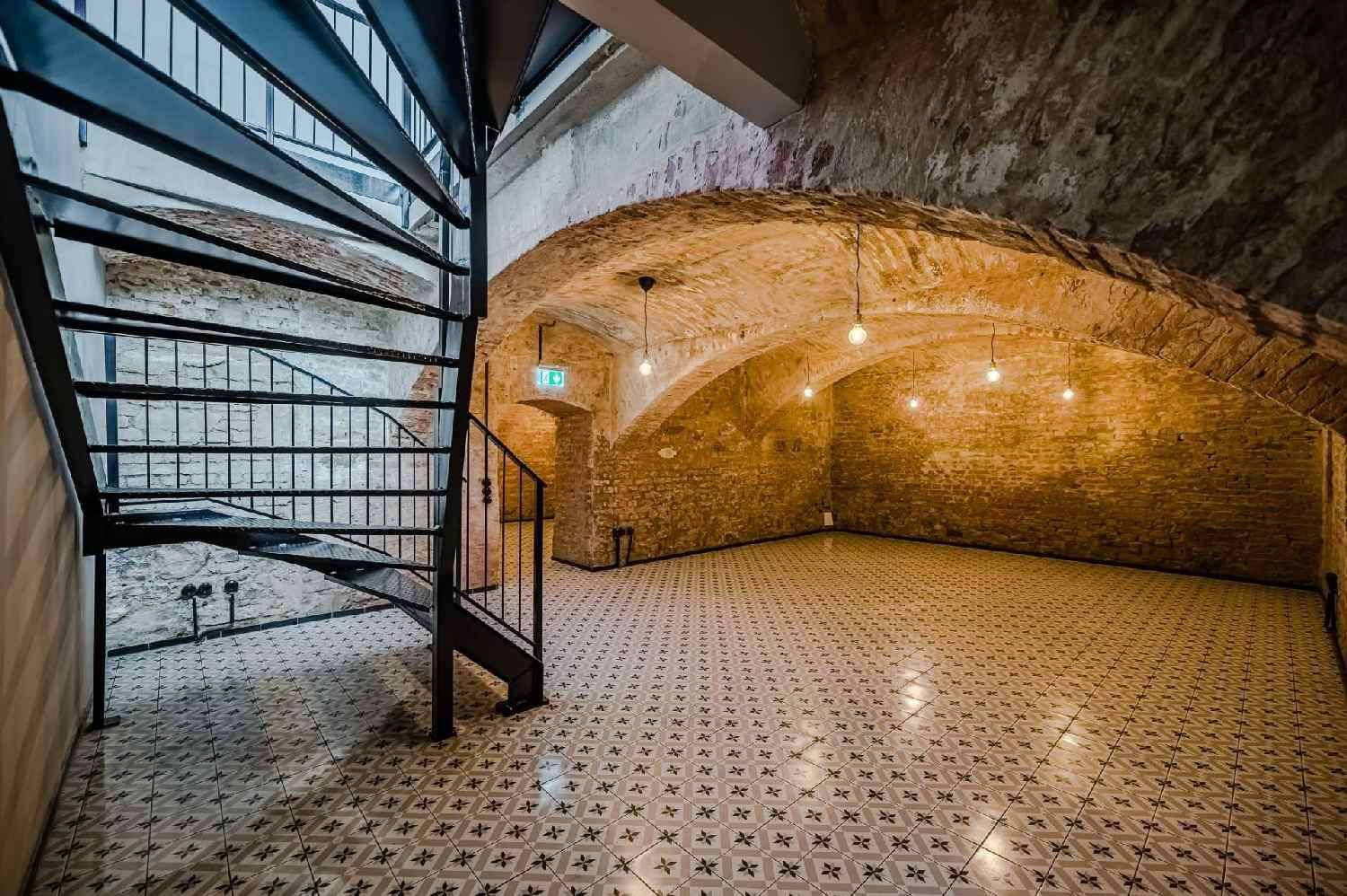 Blick auf eine Wendeltreppe in einem historischen Gewölbekeller mit Ziegelwänden und Fliesenboden.