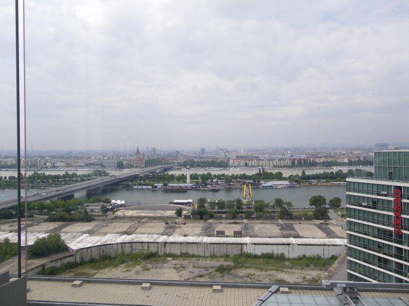Weitläufiger Blick über eine Stadt mit Fluss, Brücken und Gebäuden unter bewölktem Himmel.