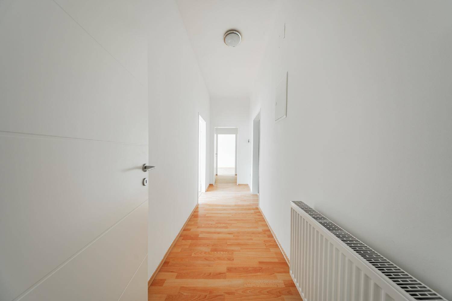 Langer, heller Flur mit Laminatboden und weiß gestrichenen Wänden, verbindet die Räume.