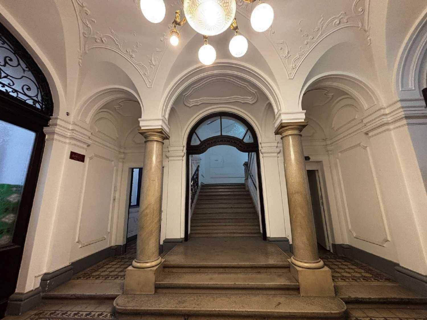 Prunkvoller Eingangsbereich eines Altbaus mit Stuckdecken, Säulen und einer eleganten Treppe.