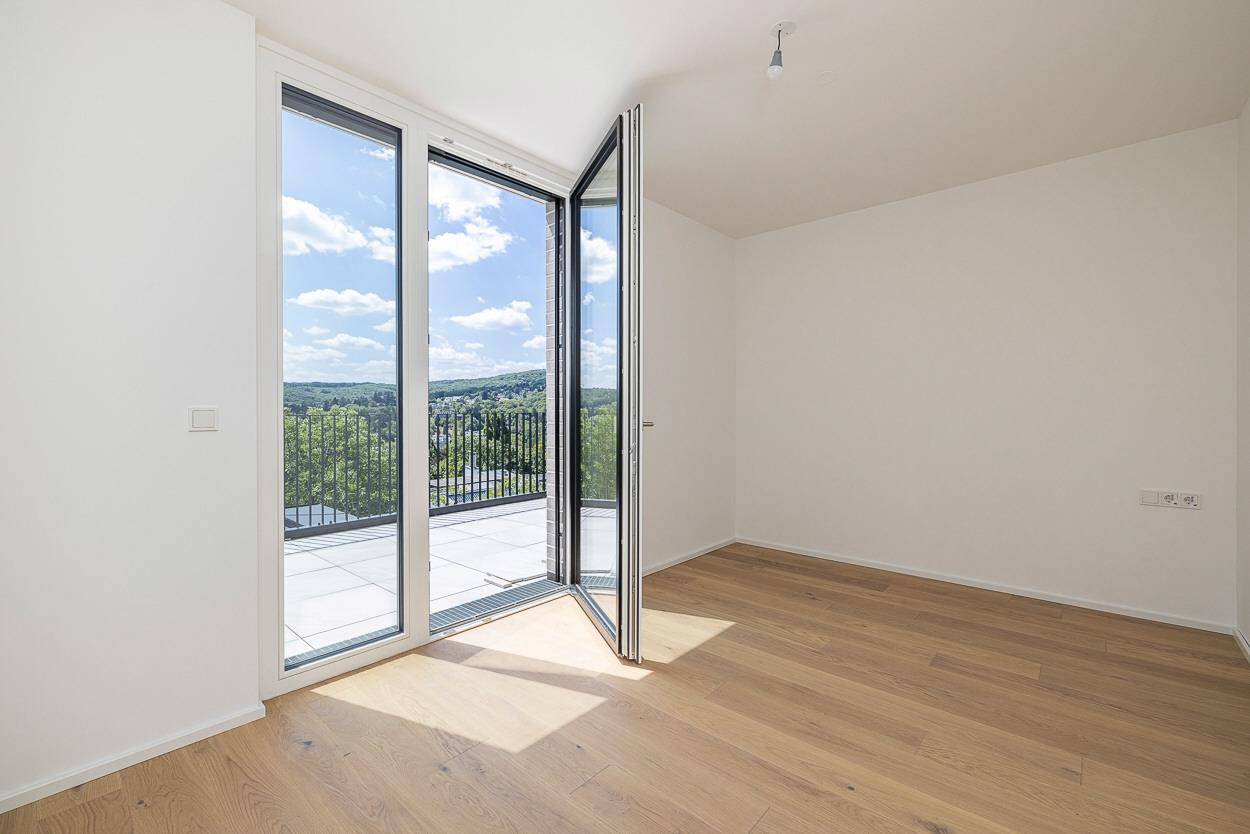 Heller Raum mit Holzboden und Zugang zu einem sonnigen Balkon mit Weitblick.
