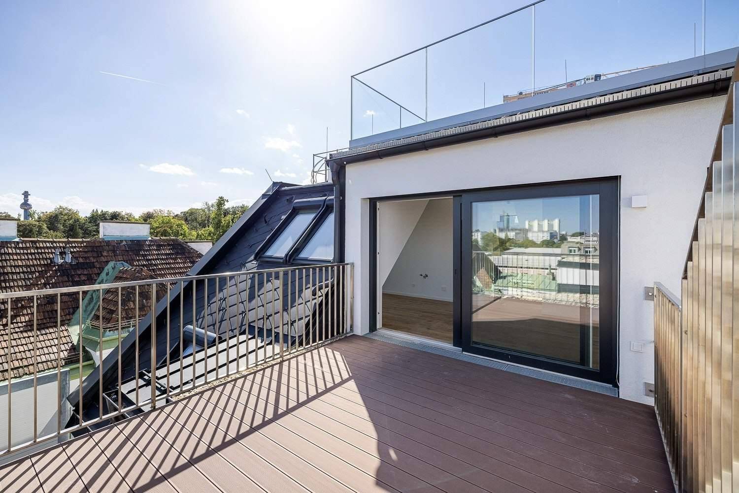 Sonnige Dachterrasse mit Holzboden, Glasgeländer und weitem Blick über die Stadt.
