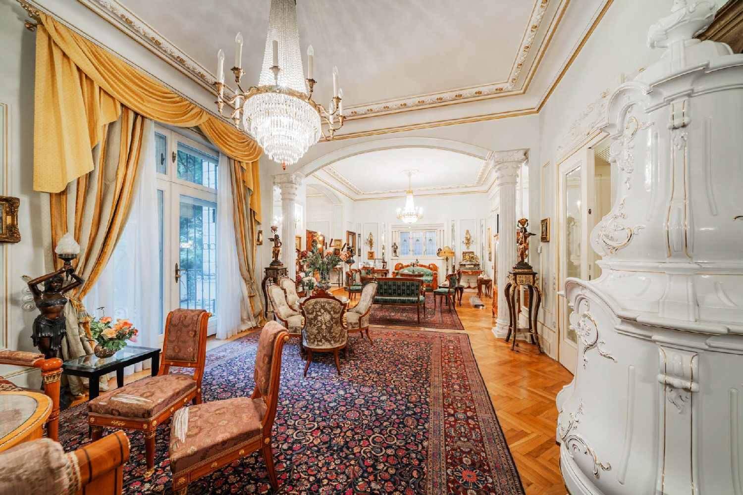 Repräsentatives Wohnzimmer mit Kachelofen, Kronleuchter und Zugang zu einem Balkon oder Garten.
