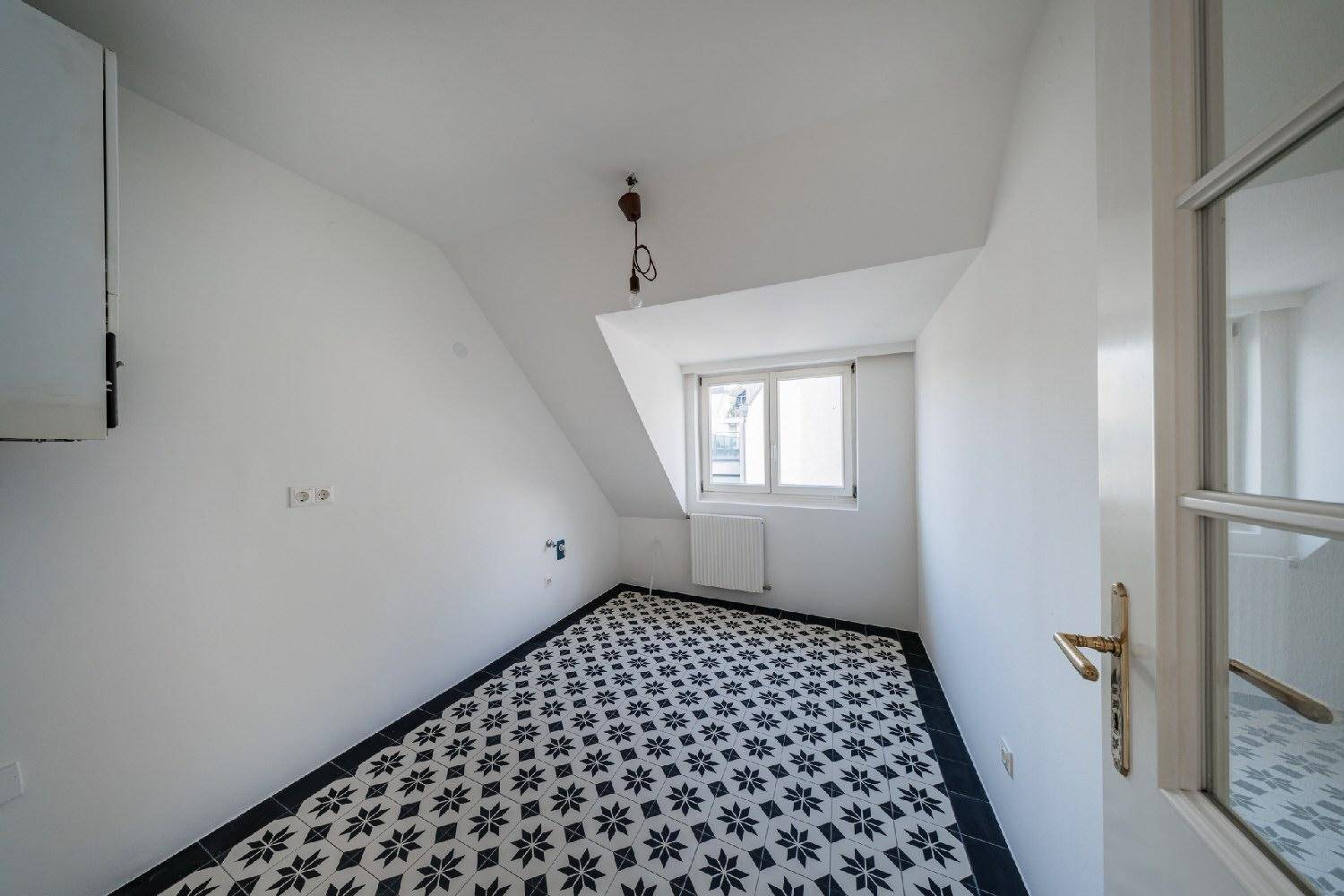 Kleiner Raum mit schrägen Wänden, gemusterten Fliesen und einem Fenster, ideal als Abstellraum.