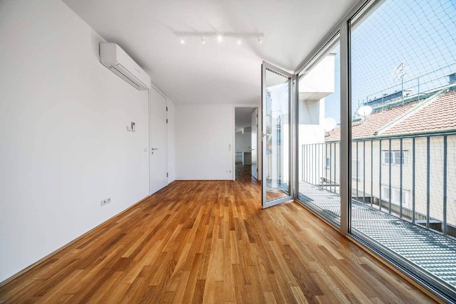 Leerer Raum mit Holzboden, Klimaanlage und großen Fenstern, die zu einem Balkon führen.