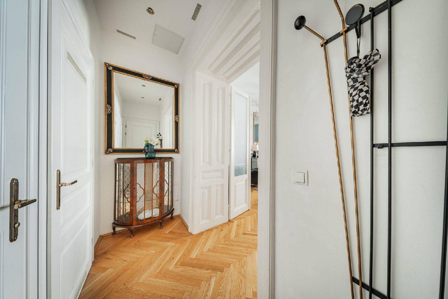 Heller Flur mit Fischgrätparkett, Spiegel und Garderobe, der zu weiteren Räumen führt.