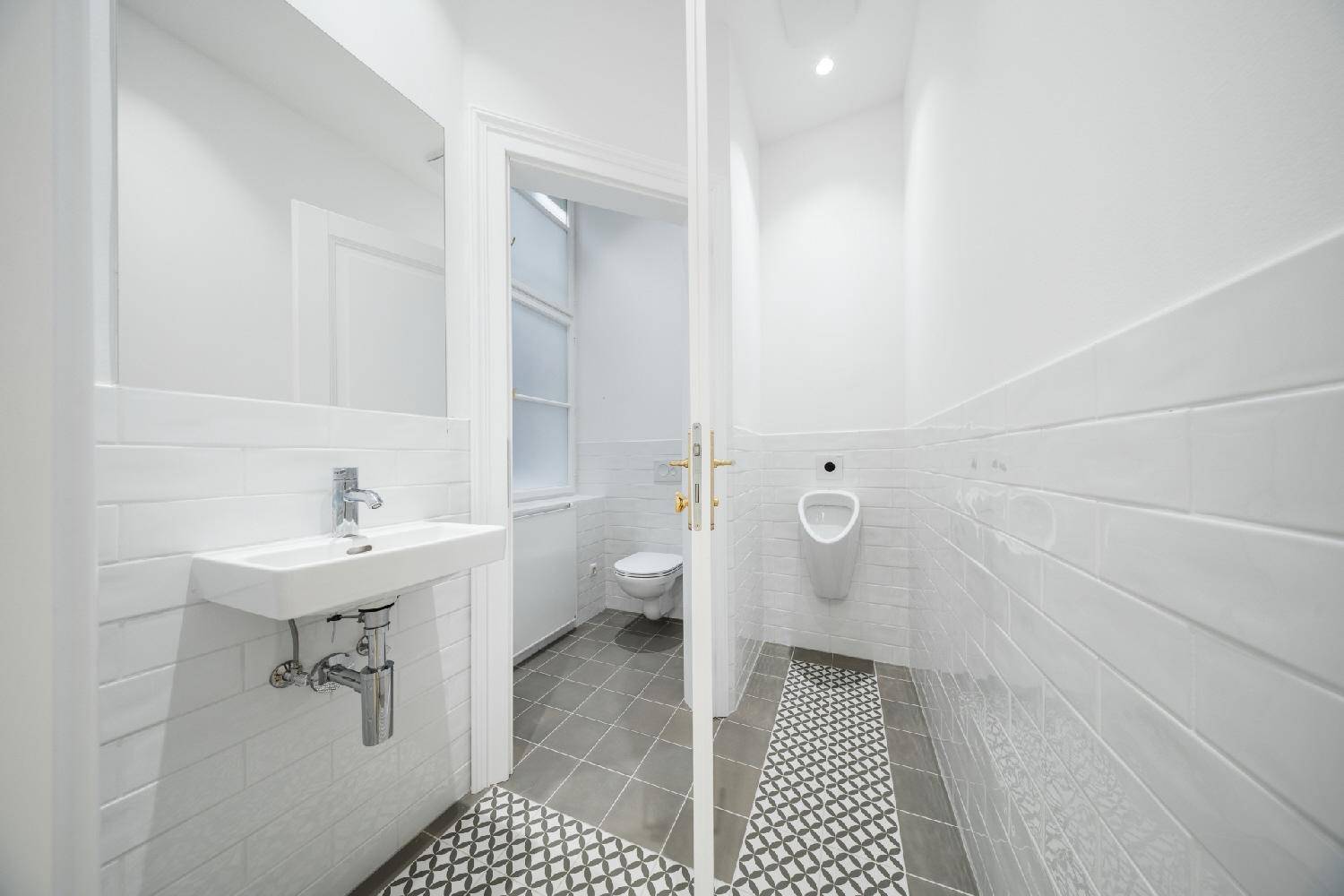 Modernes Gäste-WC mit weißen Fliesen, Waschbecken und Urinal, mit Blick auf die Toilette.