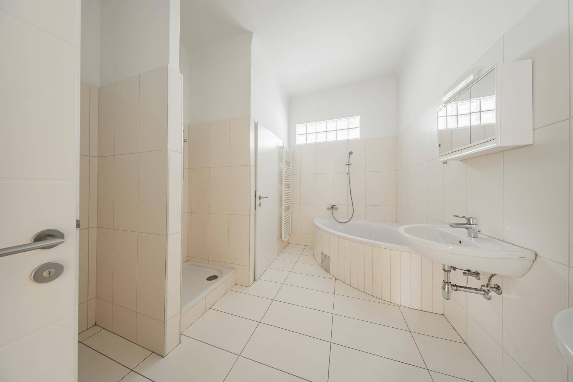 Helles Badezimmer mit Badewanne, Dusche und Waschbecken, hell gefliest und funktional.