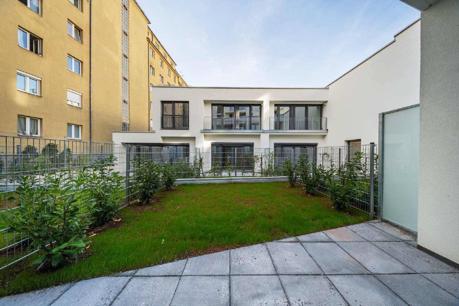 Gepflegter Gartenbereich mit Rasenfläche und gepflasterter Terrasse, umgeben von einem Zaun.