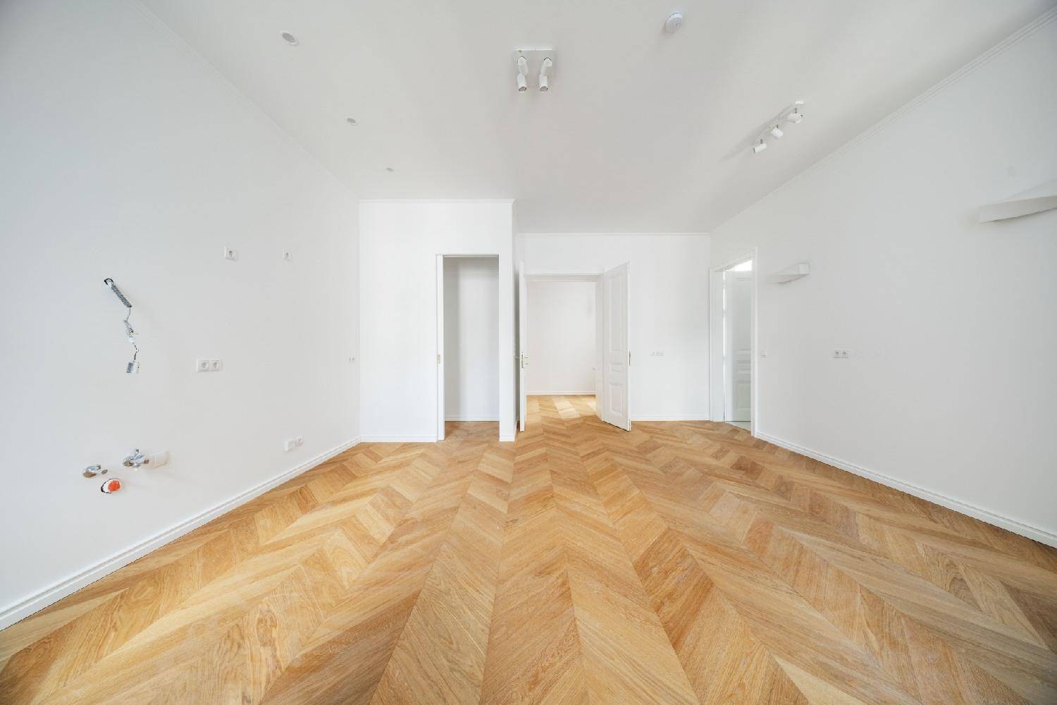 Weitläufiger, heller Raum mit Fischgrätparkett und mehreren Türen, bietet flexible Raumgestaltung.