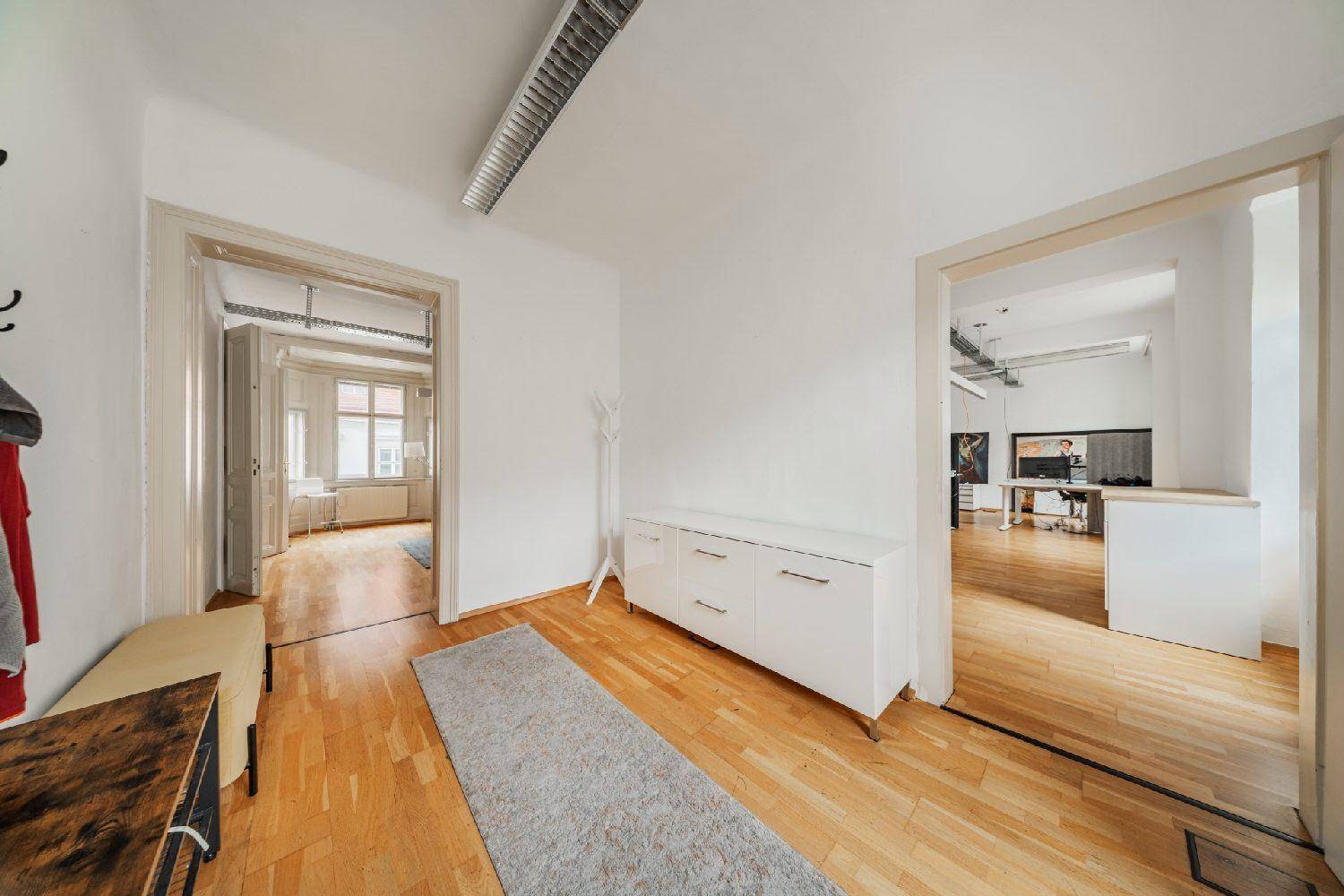 Heller Flur mit Holzboden, weißer Kommode und Garderobe, verbindet verschiedene Räume.