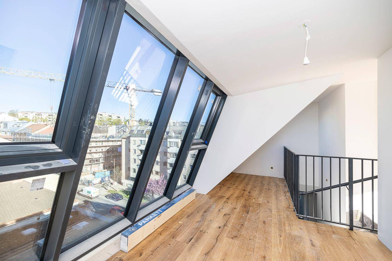 Geräumiger Dachgeschossraum mit schrägen Fenstern und Holzboden, bietet einen weiten Stadtblick.