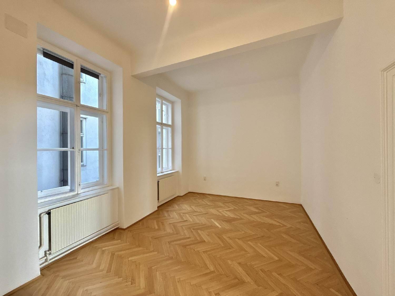Helles Zimmer mit Fischgrätparkett, zwei Fenstern und einer sichtbaren Deckenstruktur, ideal für individuelle Gestaltung.