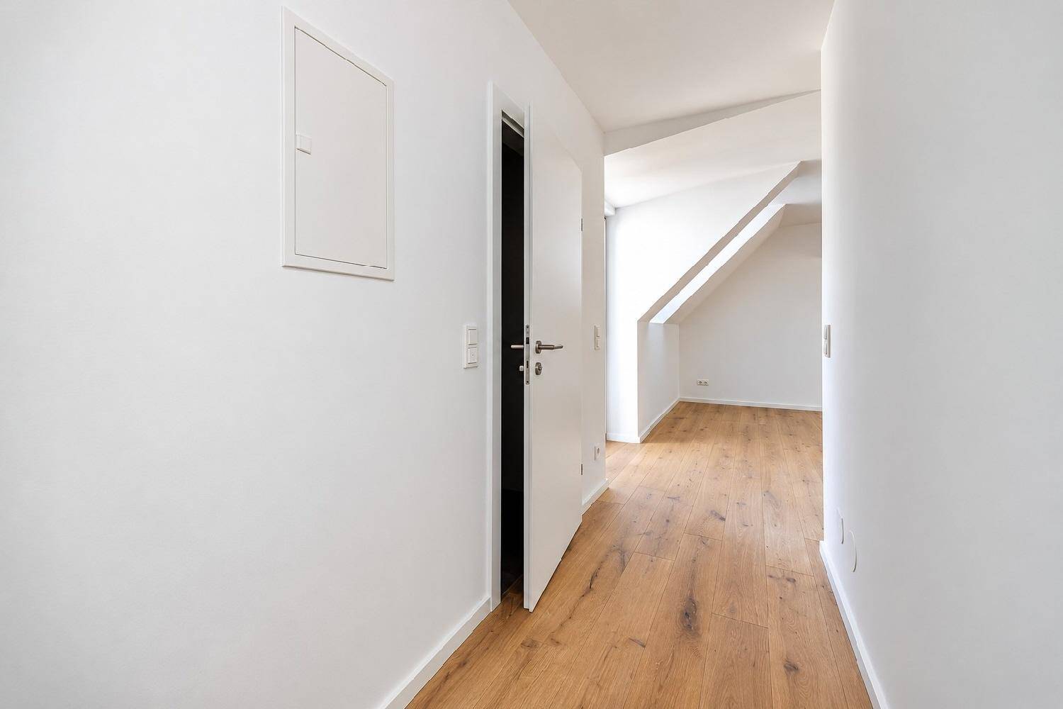 Heller Flur mit Holzboden und weißen Wänden, der zu weiteren Räumen führt.