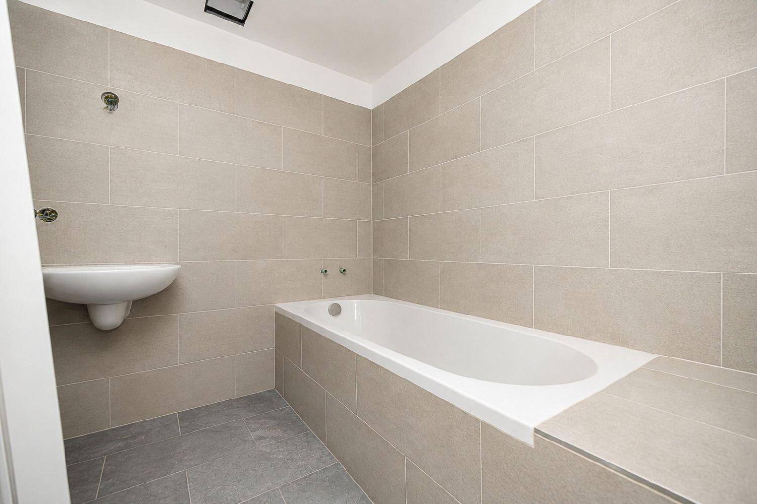 Modernes Badezimmer mit beigefarbenen Fliesen, Badewanne und wandmontiertem Waschbecken.