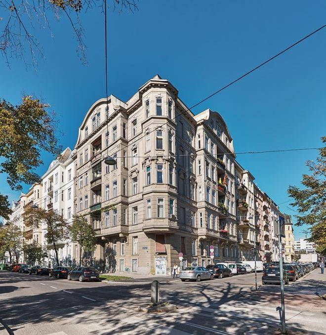 Historisches Eckgebäude mit klassischer Architektur, vielen Fenstern und Balkonen an einer belebten Straße.