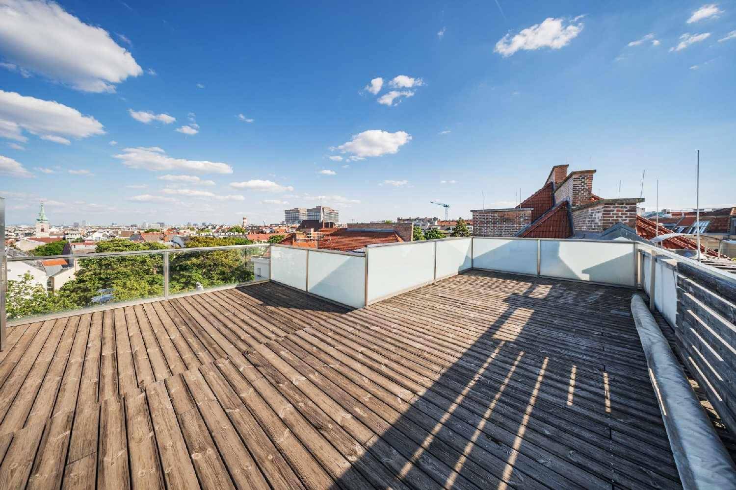 Geräumige Dachterrasse mit Holzboden und Glasgeländer, die einen Panoramablick über die Stadt bietet.