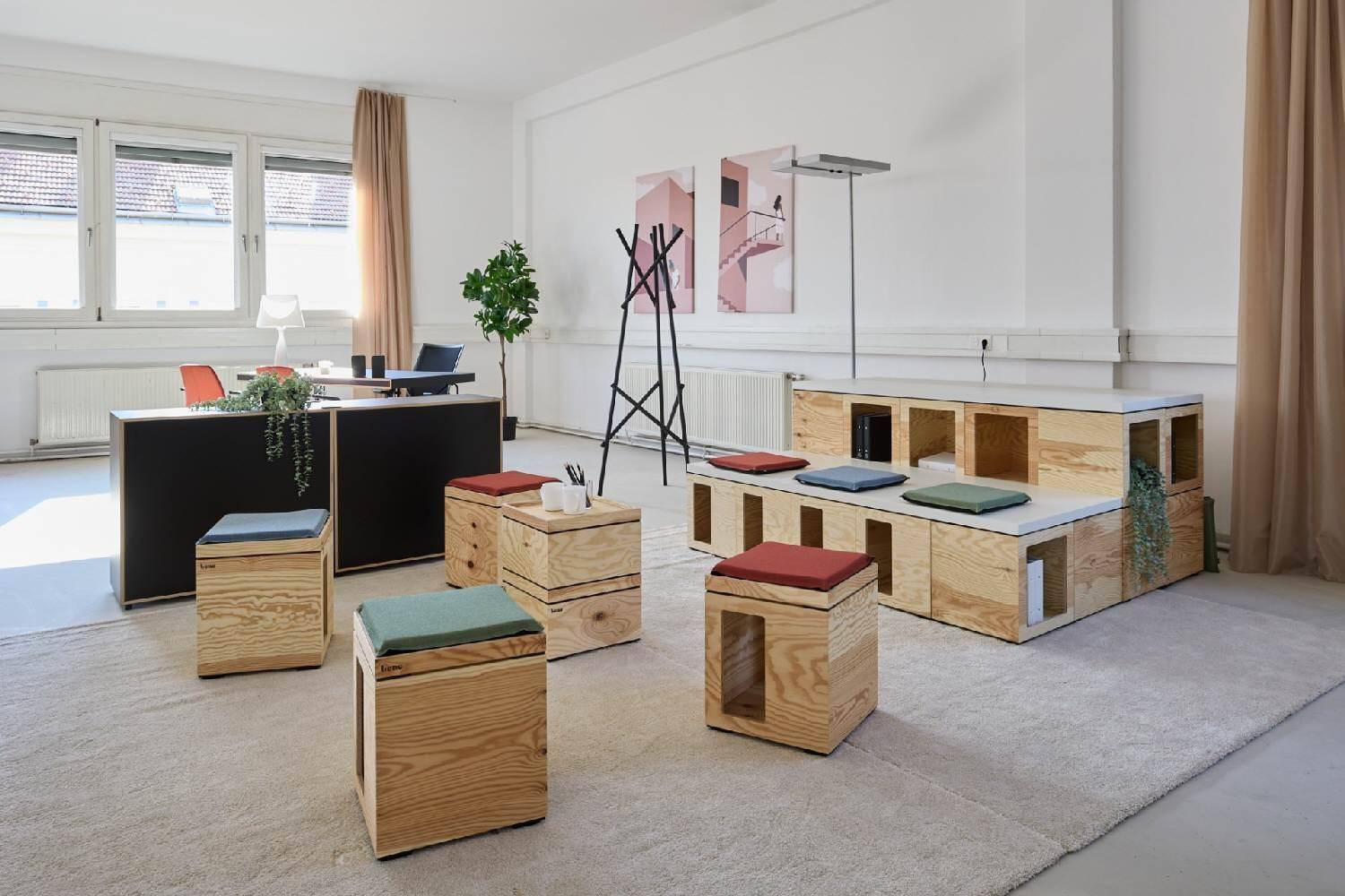 Flexibler Bürobereich mit modularen Holzelementen, Sitzhockern und einem Teppichboden.