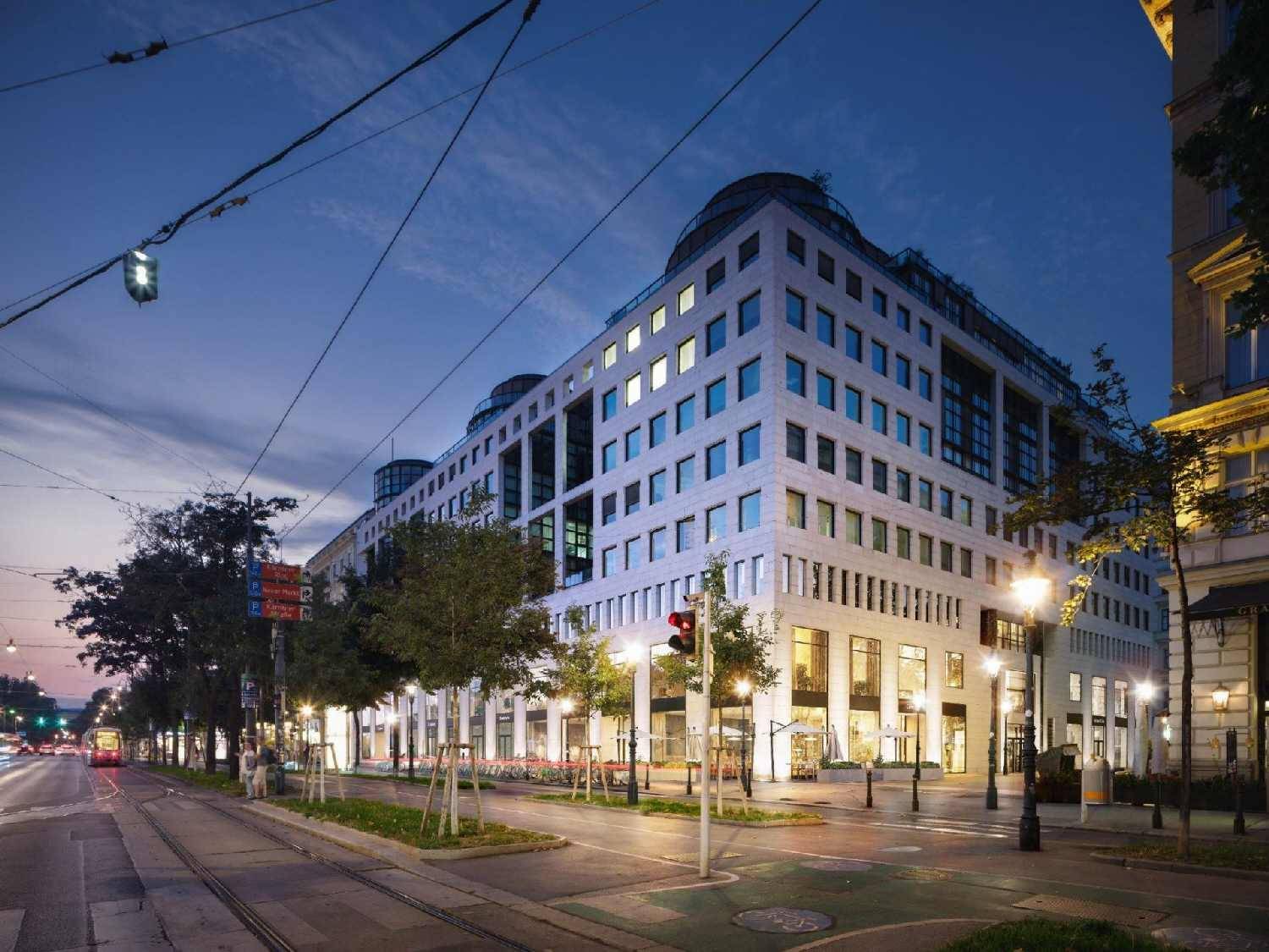 Moderne Geschäftsfassade eines Gebäudes am Abend mit beleuchteten Fenstern und Straßenbahnlinien.