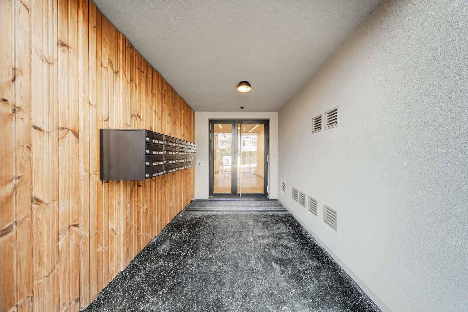Moderner Eingangsbereich mit Holzverkleidung, Briefkästen und Zugang zum Gebäude.