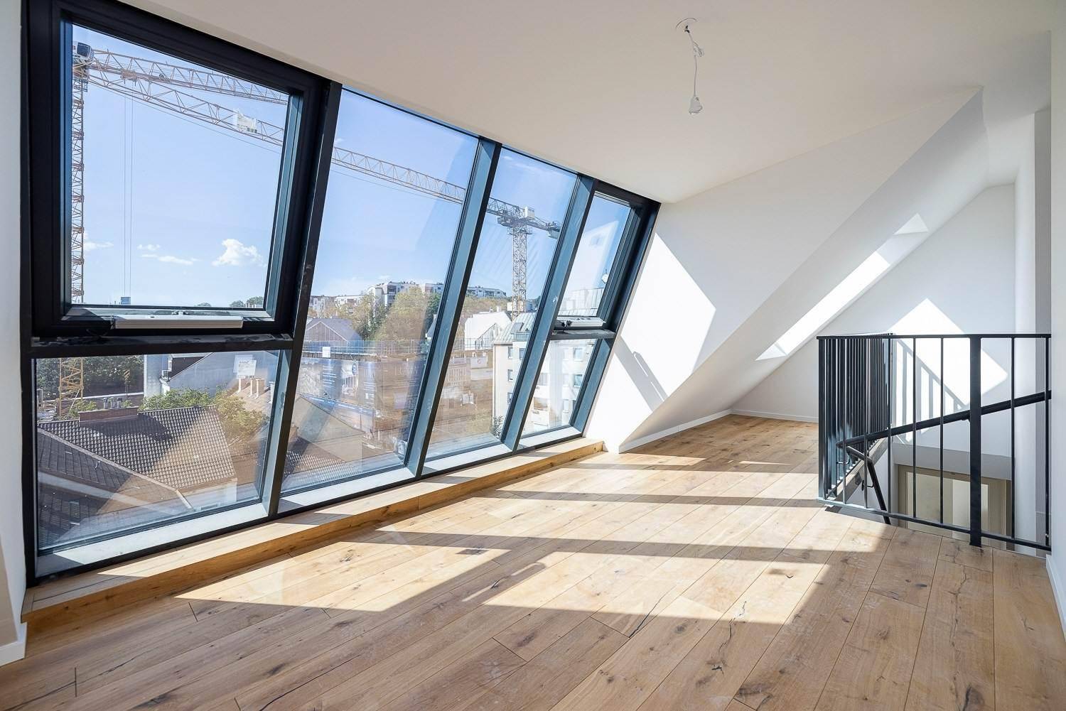 Lichtdurchflutetes Dachgeschosszimmer mit großen Schrägfenstern, Holzboden und Treppenzugang.