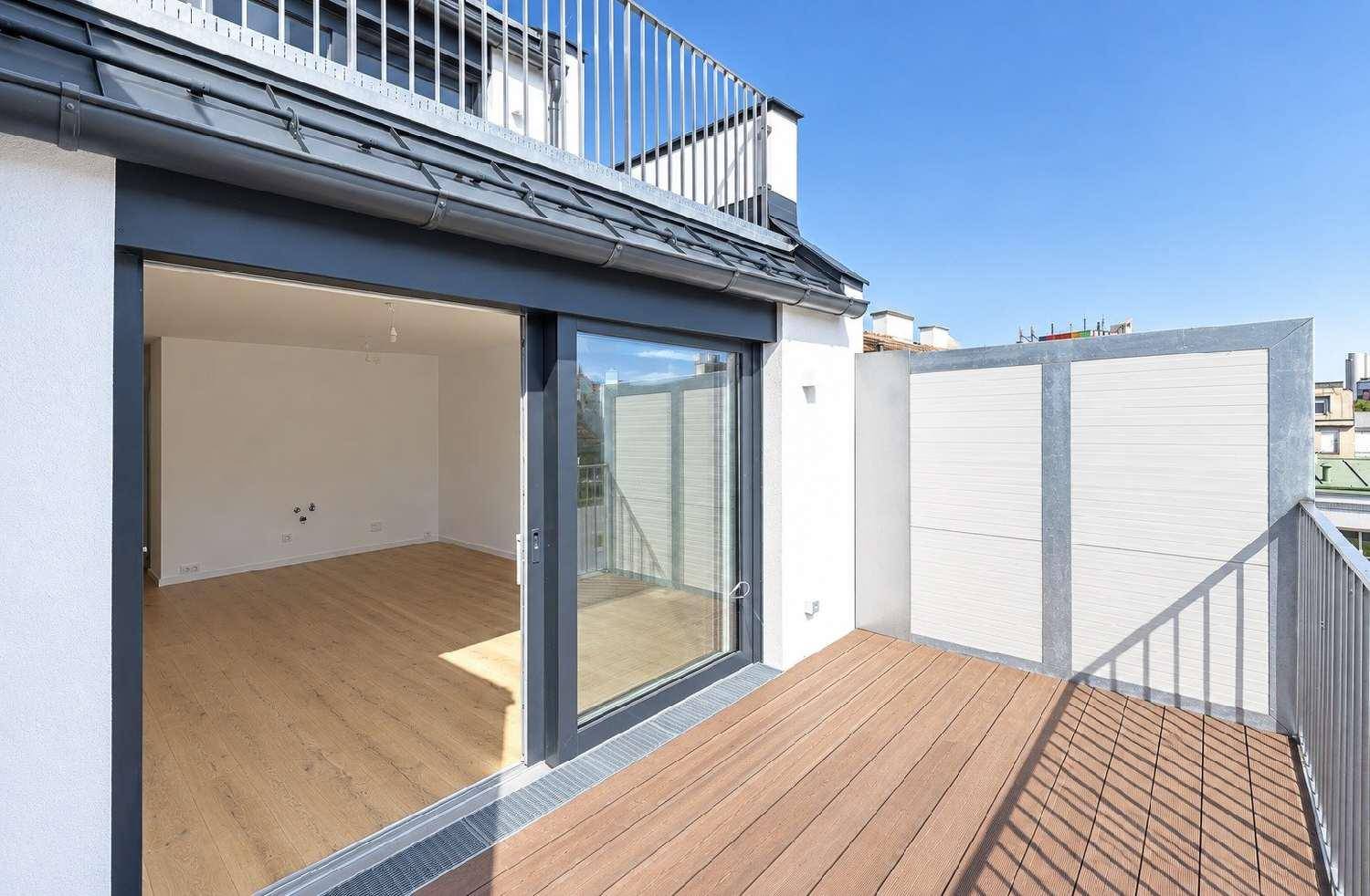 Geräumige Dachterrasse mit Holzboden und Zugang zu einem hellen Innenraum unter blauem Himmel.
