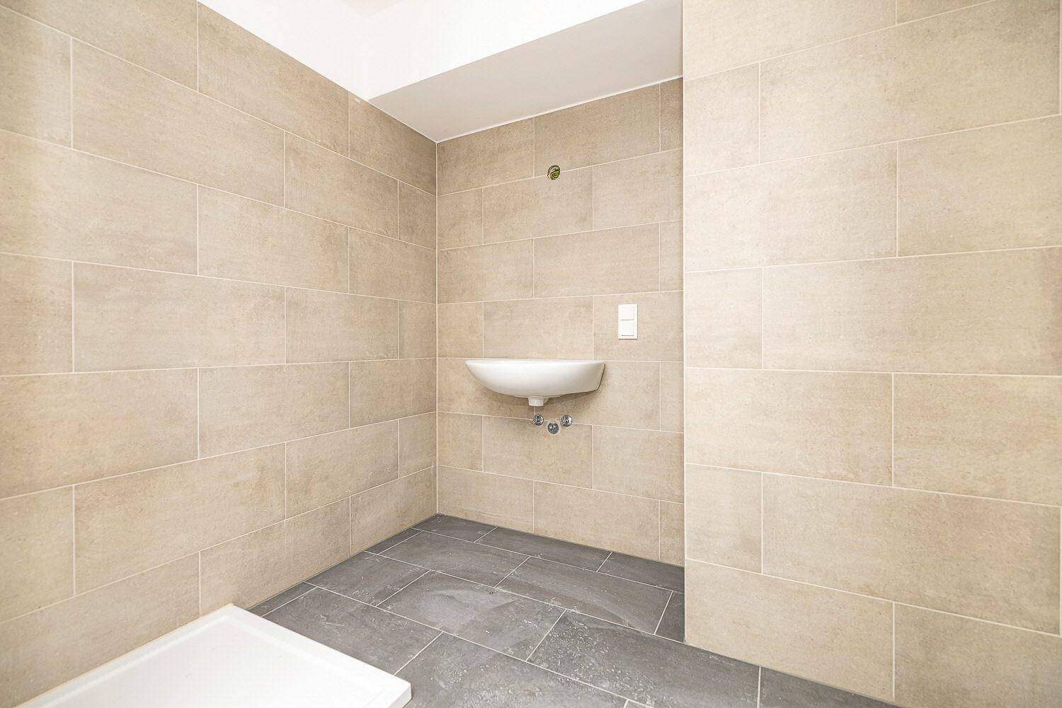 Modernes Badezimmer im Bau mit beigefarbenen Wandfliesen, grauen Bodenfliesen und einem Waschbecken.
