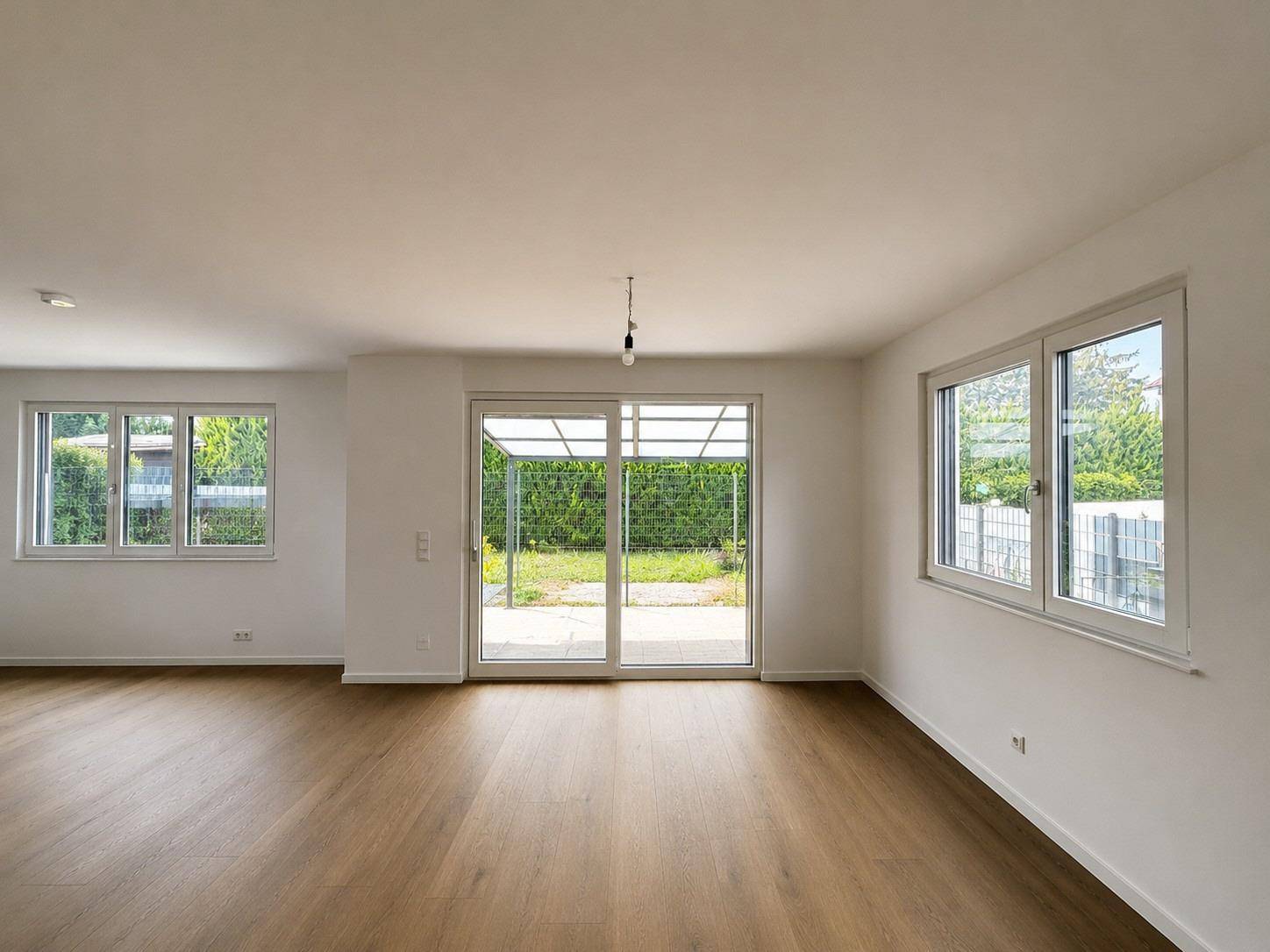 Geräumiges Wohnzimmer mit Holzboden, großen Fenstern und Zugang zum Garten.