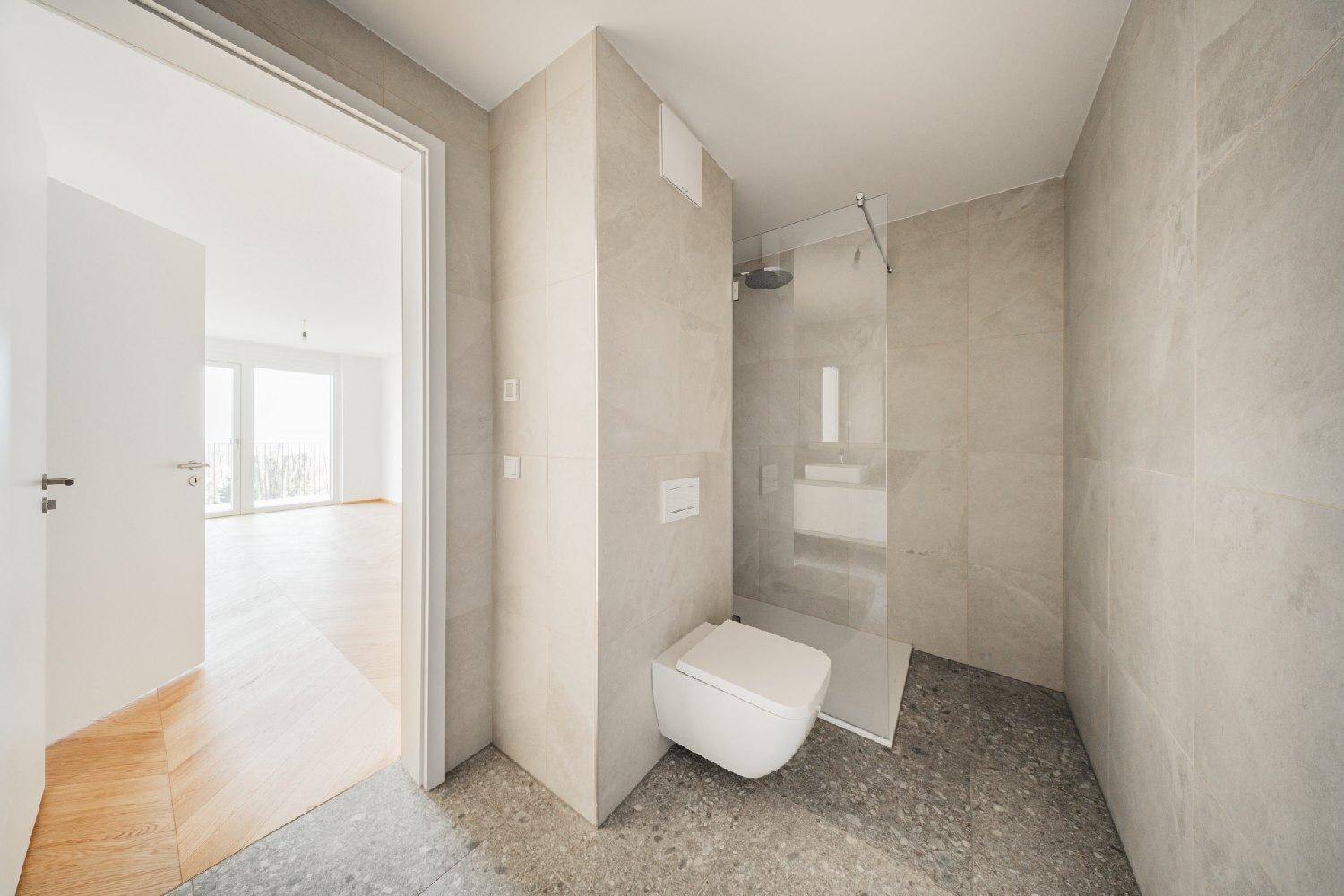 Modernes Badezimmer mit begehbarer Dusche, Wand-WC und hellen Fliesen an Wänden und Boden.
