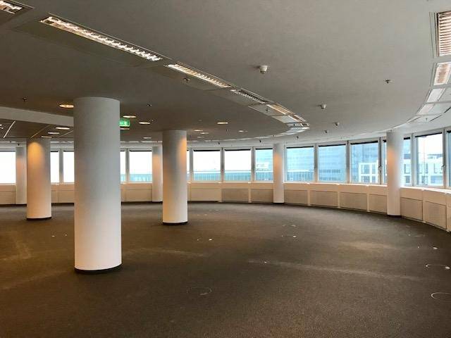 Großer, offener Büroraum mit Teppichboden, vielen Fenstern und Säulen, bereit für die Gestaltung.