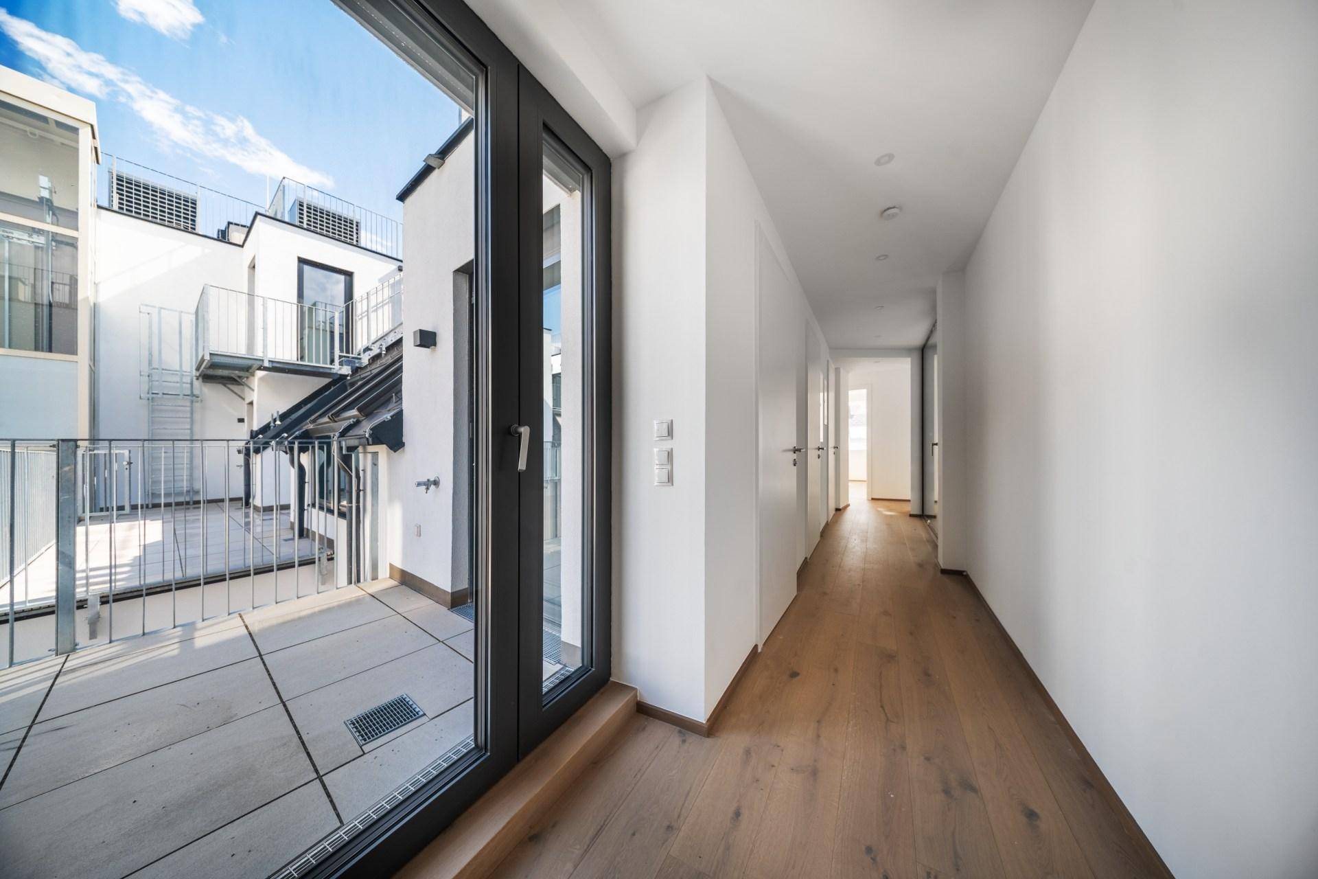 Heller Flur mit Holzboden und Zugang zu einem Außenbereich mit Blick auf moderne Gebäude.