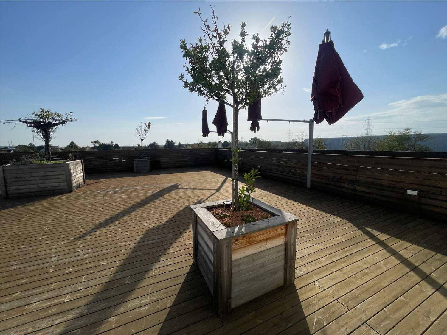 Geräumige Dachterrasse mit Holzboden, bepflanzten Hochbeeten und Sonnenschirm unter blauem Himmel.