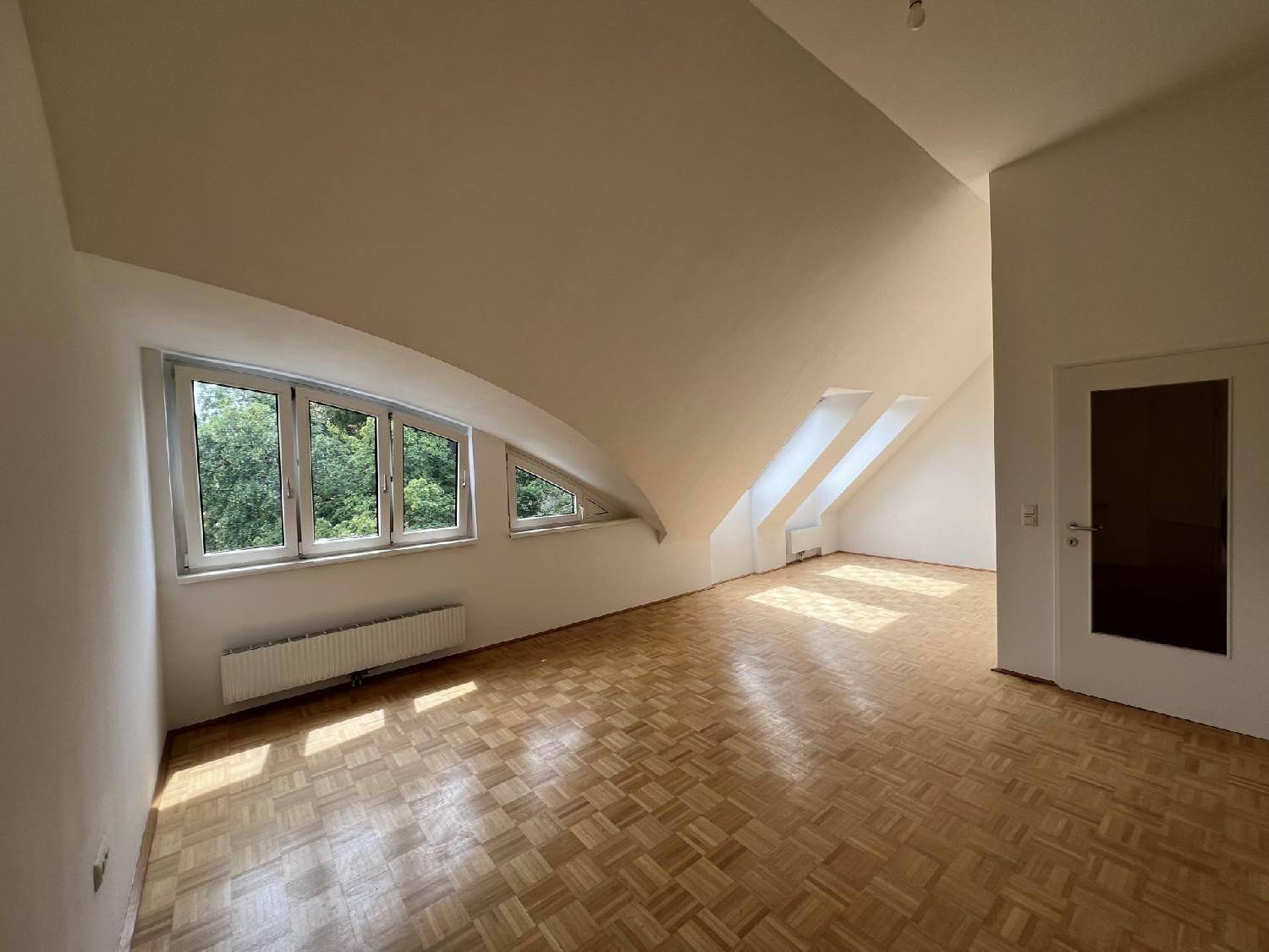 Heller Wohnraum mit Parkettboden, Dachschrägen und viel natürlichem Licht durch Fenster.