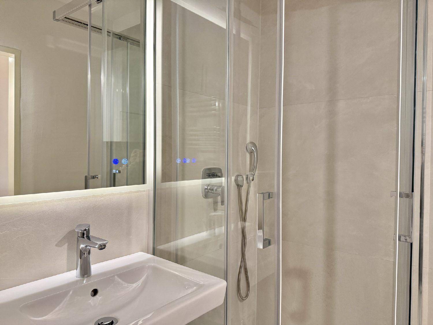 Modernes Badezimmer mit Duschkabine, Waschbecken und beleuchtetem Spiegelschrank.