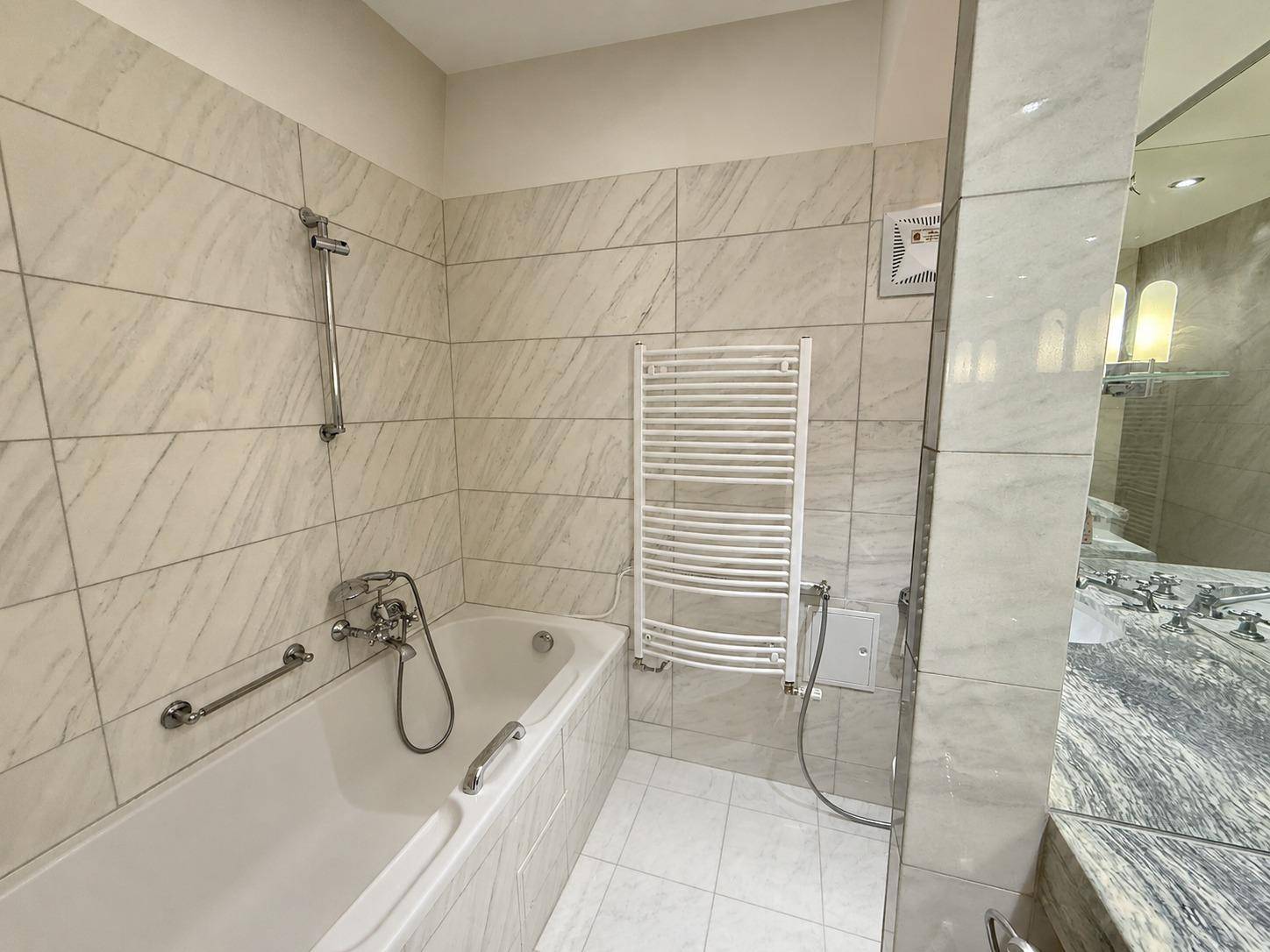Modern gefliestes Badezimmer mit Badewanne, Duscharmatur und beheiztem Handtuchhalter.